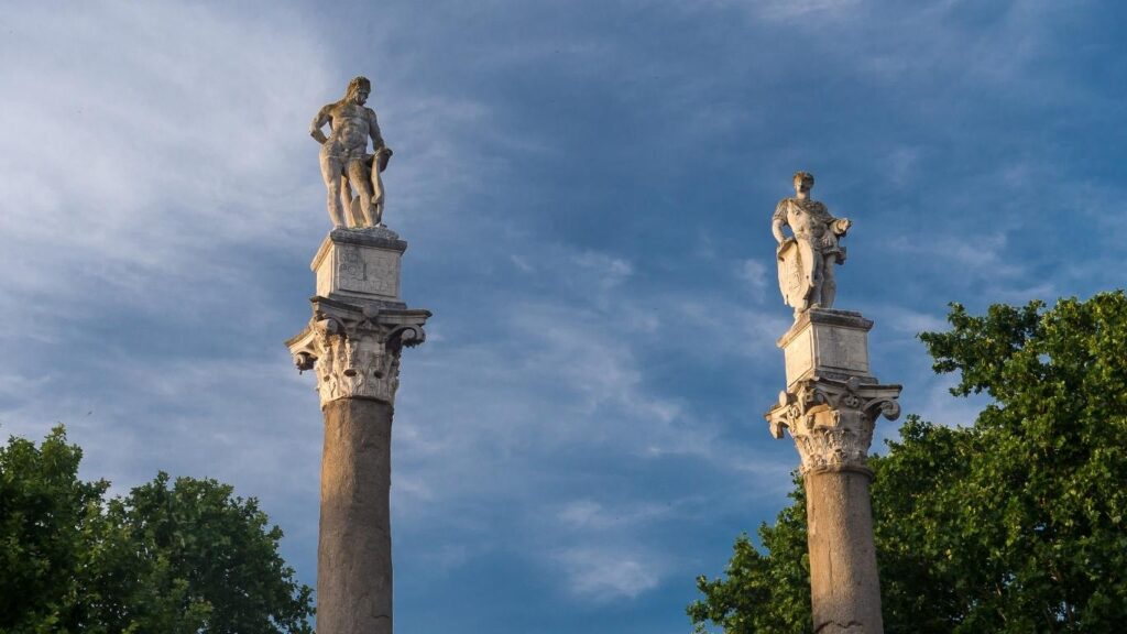 Columnas romanas con estatuas de Hércules y Julio César en la Alameda de Hércules de Sevilla, bajo un cielo azul al atardecer.