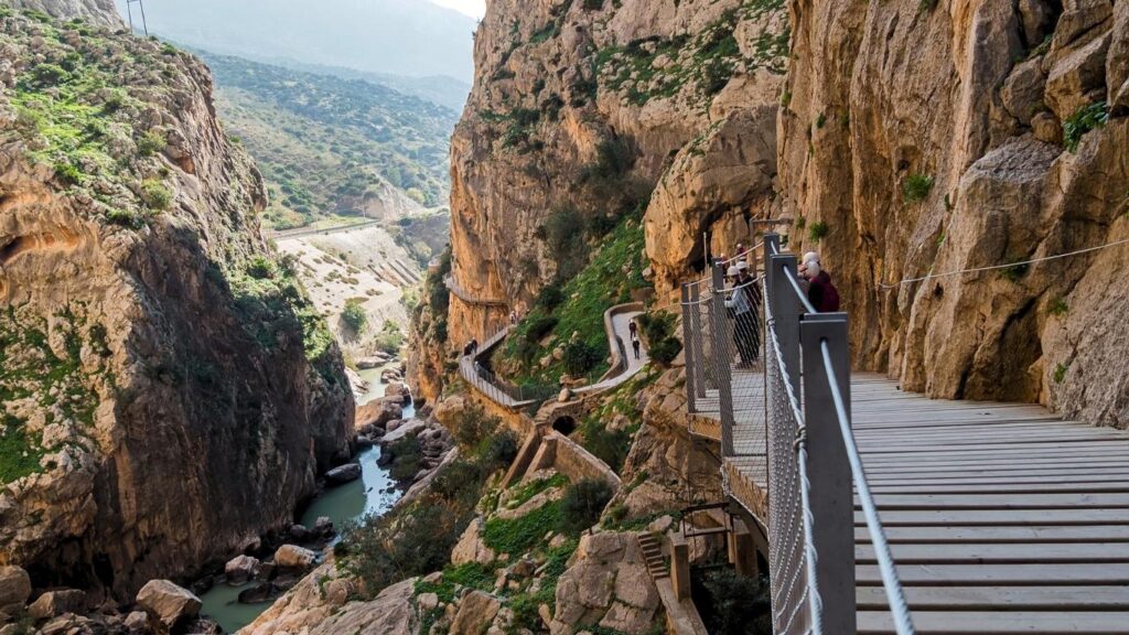 Pasarela del Caminito del Rey suspendida entre paredes de roca escarpadas y un río en un desfiladero soleado.