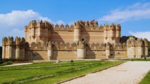 Vista panorámica del Castillo de Coca en Segovia, destacando sus fosos y el contraste de su arquitectura de ladrillo con el entorno.