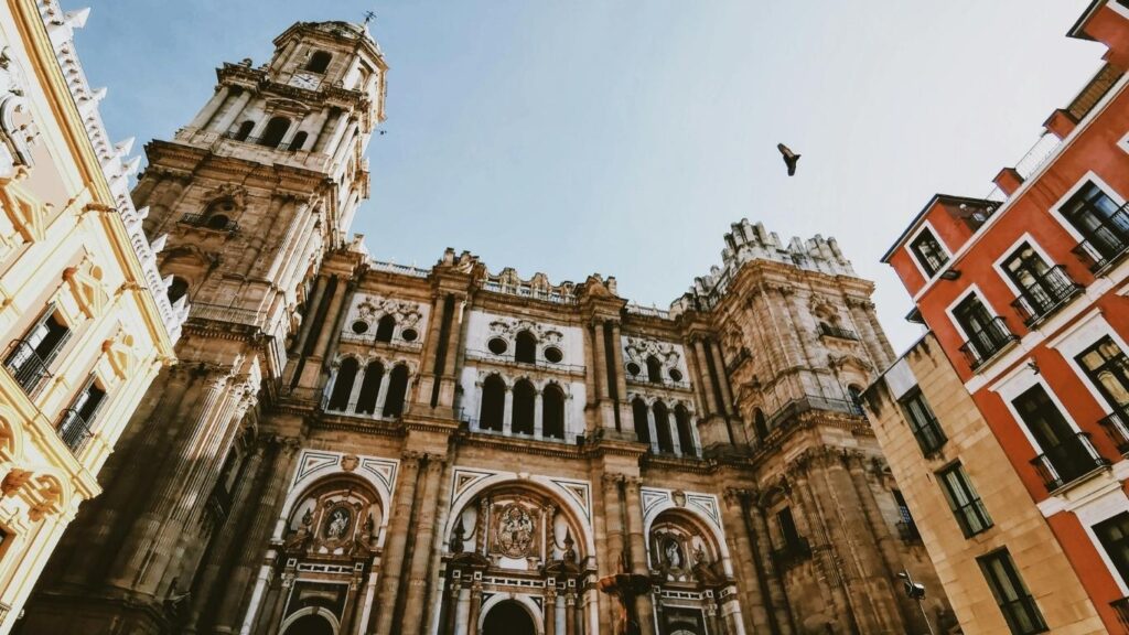 Fachada renacentista de la Catedral de Málaga "La Manquita", con su única torre visible, bajo un cielo azul y flanqueada por edificios.
