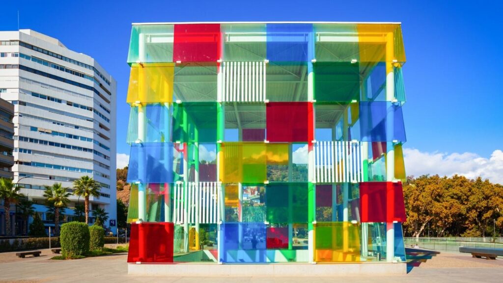 Fachada de un edificio moderno de forma cúbica con paneles de cristal de colores en el Muelle Uno de Málaga en invierno, bajo un cielo azul.