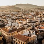 Vista panorámica de los tejados del centro histórico de Málaga en invierno con edificios blancos y montañas en el horizonte al atardecer.