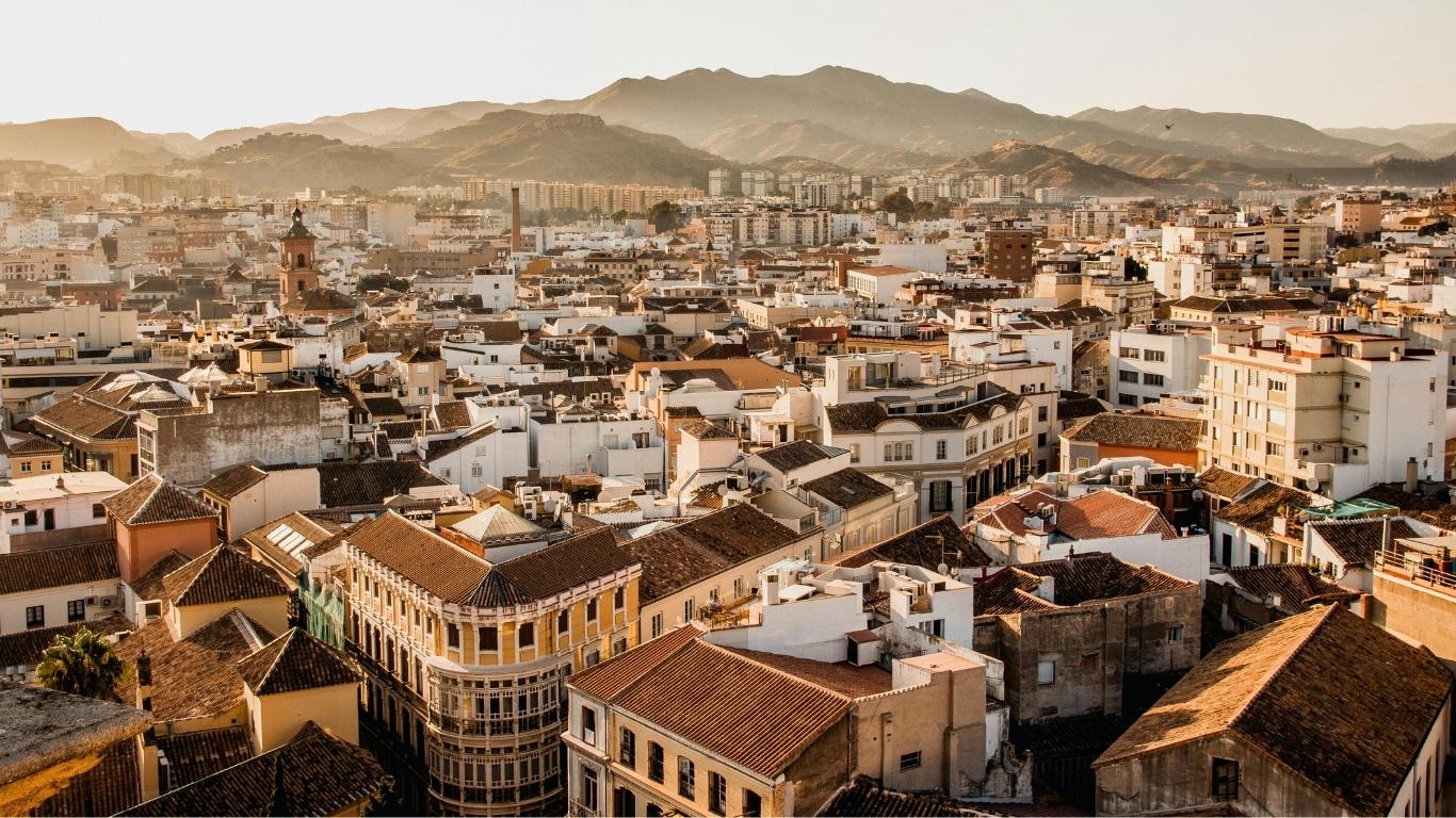 Vista panorámica de los tejados del centro histórico de Málaga en invierno con edificios blancos y montañas en el horizonte al atardecer.