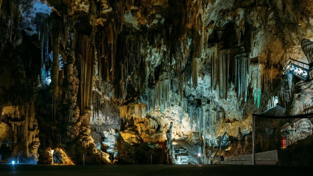 Interior de las Cuevas de Nerja con formaciones rocosas (estalactitas y estalagmitas) iluminadas en tonos cálidos y fríos, creando un paisaje subterráneo.