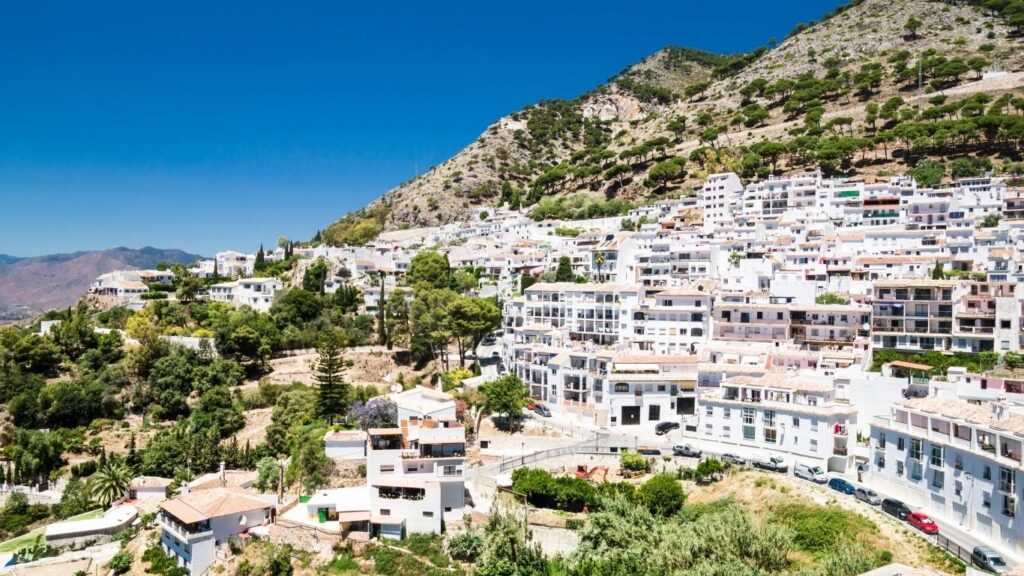 Vista panorámica de Mijas Pueblo, con sus casas blancas escalonadas en la ladera de una montaña verde, bajo un cielo azul brillante.