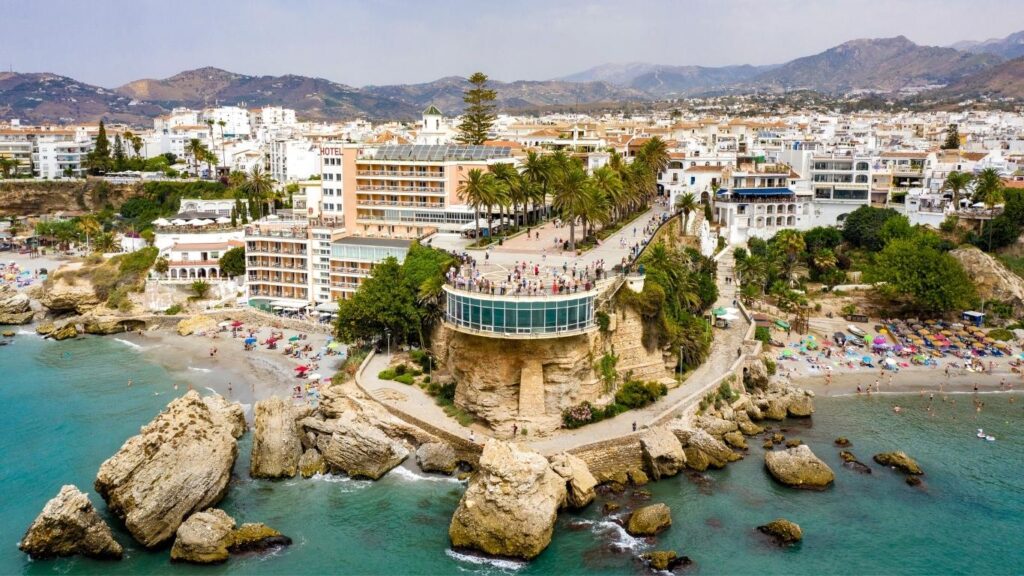 Vista aérea del Balcón de Europa en Nerja, un mirador con palmeras que sobresale hacia el mar Mediterráneo, rodeado de playas.