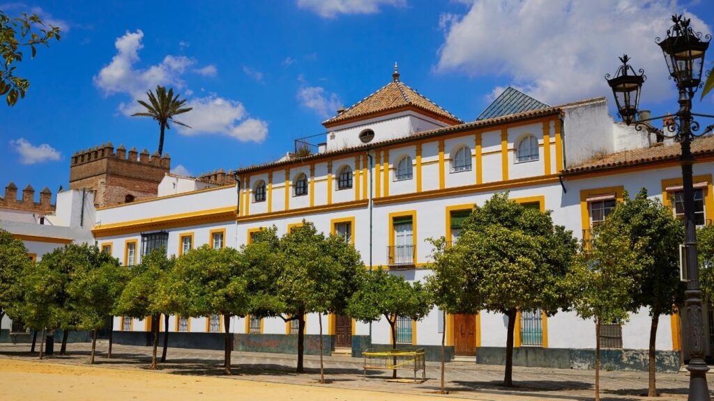 Edificios tradicionales de fachadas blancas y amarillas en el Patio de Banderas, con una vista parcial de la muralla del Real Alcázar al fondo.
