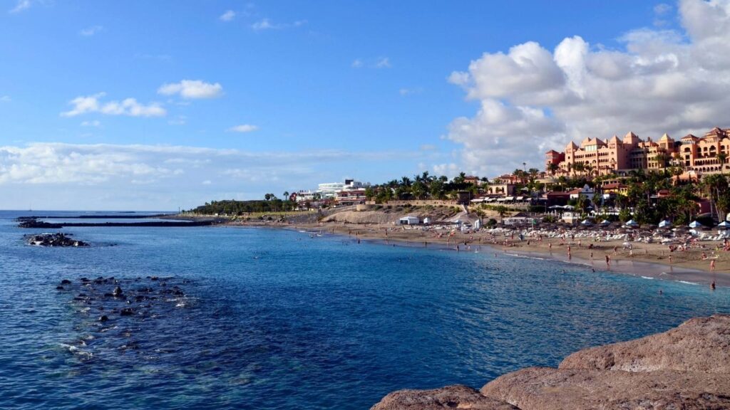 Playa del Duque en Costa Adeje, Tenerife, con arena dorada y hoteles de lujo, reflejando su estatus de playa resguardada