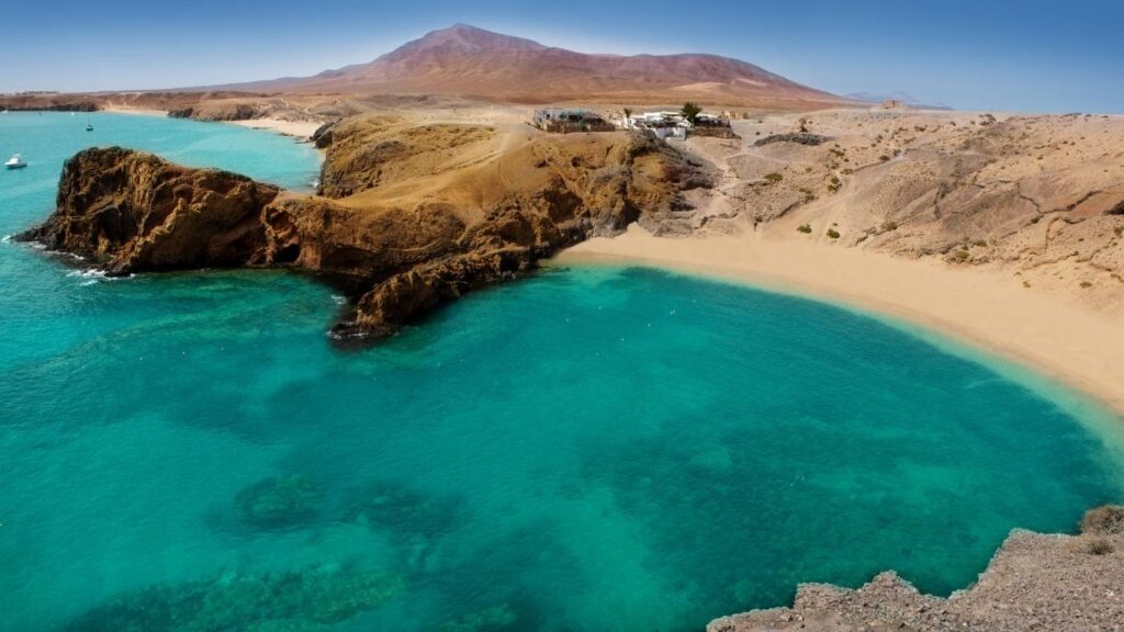 Cala de Playa Papagayo en Lanzarote con aguas turquesas intensas, arena dorada y colinas desérticas al fondo.