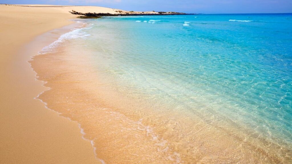 Extensión de arena clara en las Grandes Playas de Corralejo, Fuerteventura, con agua cristalina y turquesa.