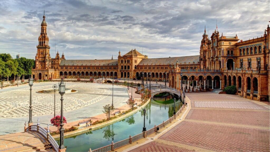 Vista panorámica del edificio principal de la Plaza de España en Sevilla, con el canal, los puentes y la torre sur bajo un cielo nublado. Una parada esencial en tu ruta de Sevilla en 3 días.