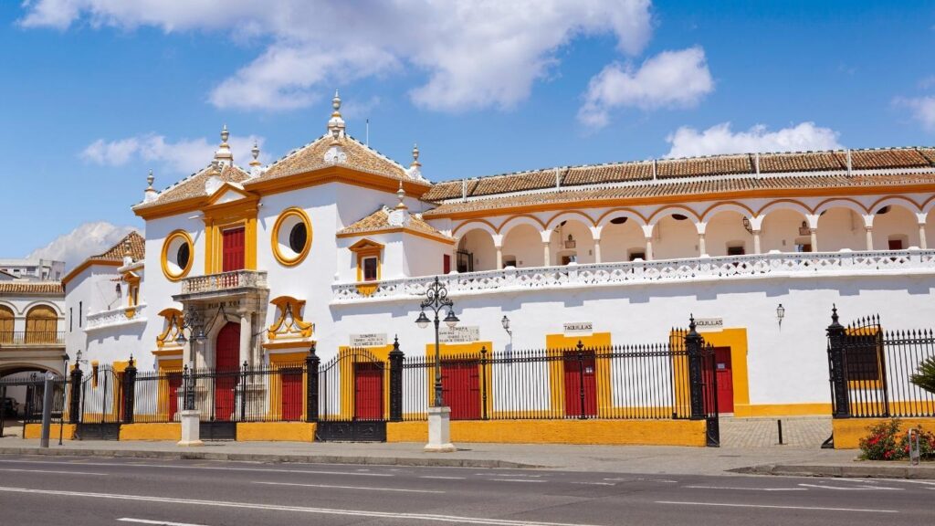Fachada blanca y amarilla de la Plaza de Toros de la Real Maestranza de Caballería de Sevilla bajo un cielo azul.