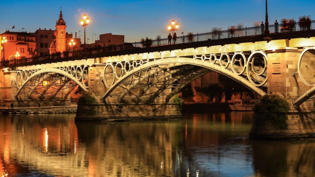 El Puente de Isabel II (Puente de Triana) iluminado sobre el río Guadalquivir al anochecer en Sevilla.