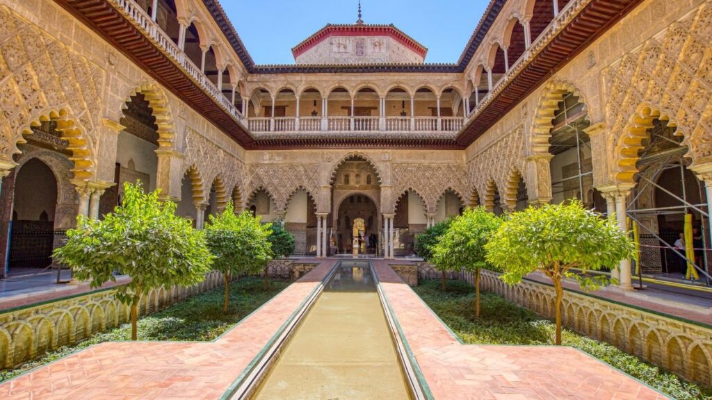 El Patio de las Doncellas del Real Alcázar de Sevilla, con arquitectura mudéjar, arcos de herradura y un estanque central.