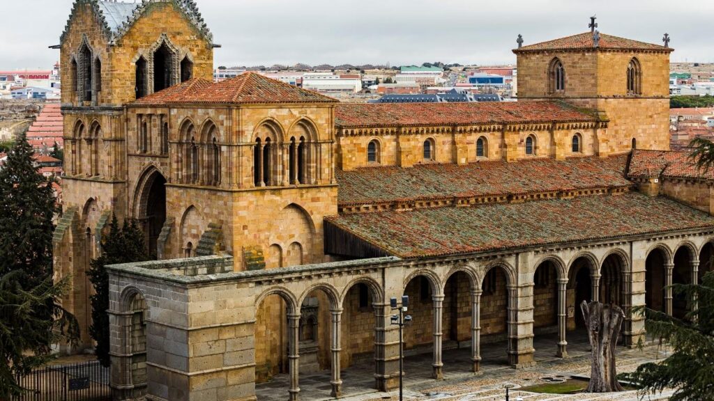 Vista aérea parcial de la Real Basílica de San Vicente en Ávila, mostrando su robusta construcción en piedra rojiza y sus arcadas románicas. Hito de la Ruta del Románico castellano.