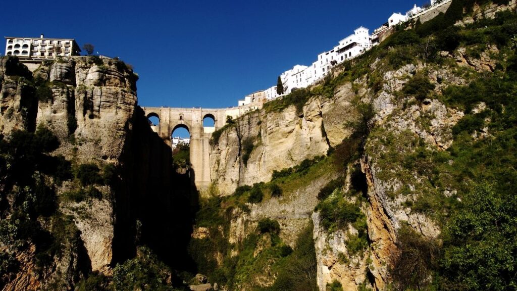 Vista del icónico Puente Nuevo de Ronda, uniendo la ciudad a través del profundo cañón de El Tajo, con casas blancas en el borde superior.