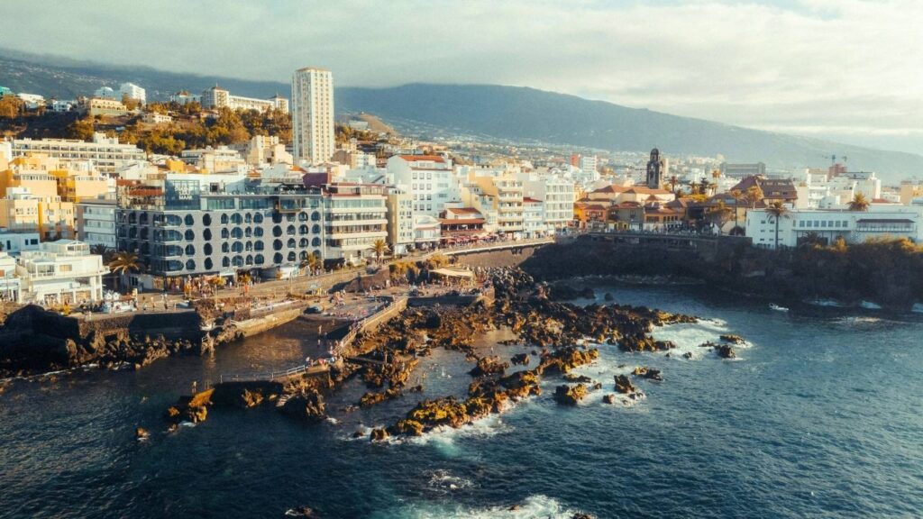 Vista de la costa urbana de Santa Cruz de Tenerife con edificios modernos, una zona rocosa y el océano.