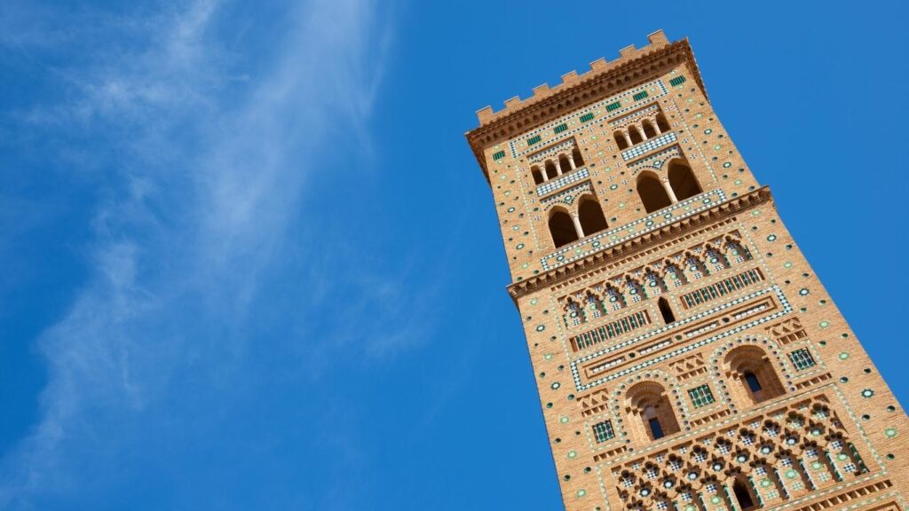La elegante Torre de San Martín de Teruel contra el cielo azul, mostrando sus arcos y la característica cerámica vidriada del mudéjar.
