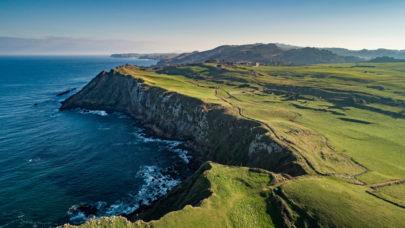 Acantilados de la Costa Quebrada en Cantabria en invierno, con prados verdes frente al Mar Cantábrico bajo un cielo despejado.