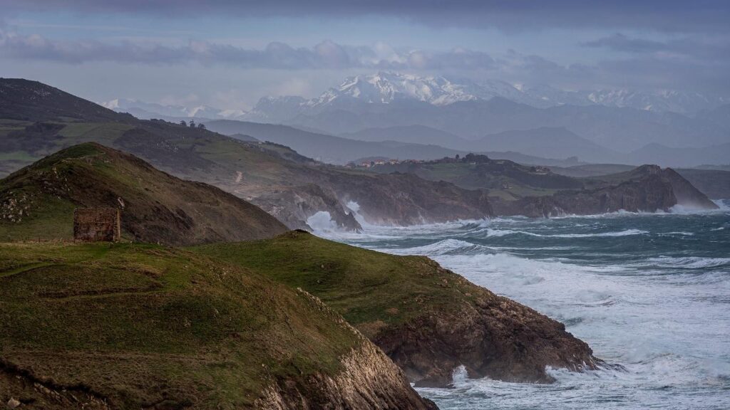 Olas rompiendo en Tagle con la silueta de los Picos de Europa nevados al fondo.
