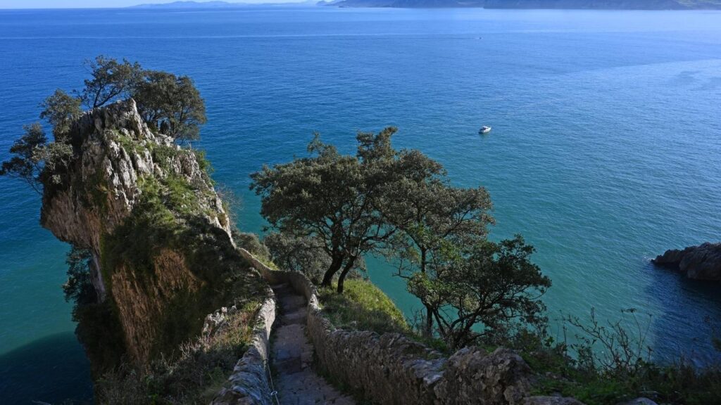 Escaleras de piedra que bajan por el acantilado hacia el Faro del Caballo en Santoña con vistas al mar Cantábrico.