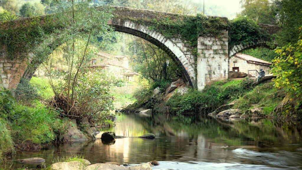 Puente de piedra de estilo romano en Liérganes, Cantabria, rodeado de vegetación y reflejado en el río.