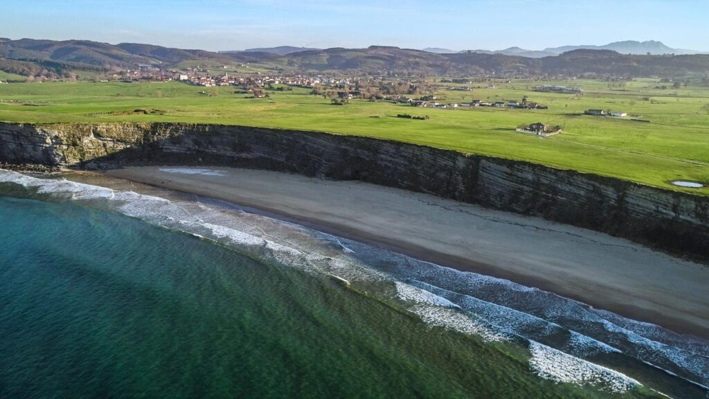 Vista aérea de la Playa de Langre en Cantabria con sus característicos acantilados verticales y prados verdes junto al mar.