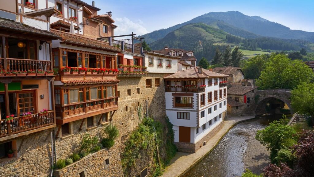 Vistas del pueblo de Potes en Cantabria con casas tradicionales de piedra, balcones de madera y el río Deva con montañas al fondo.