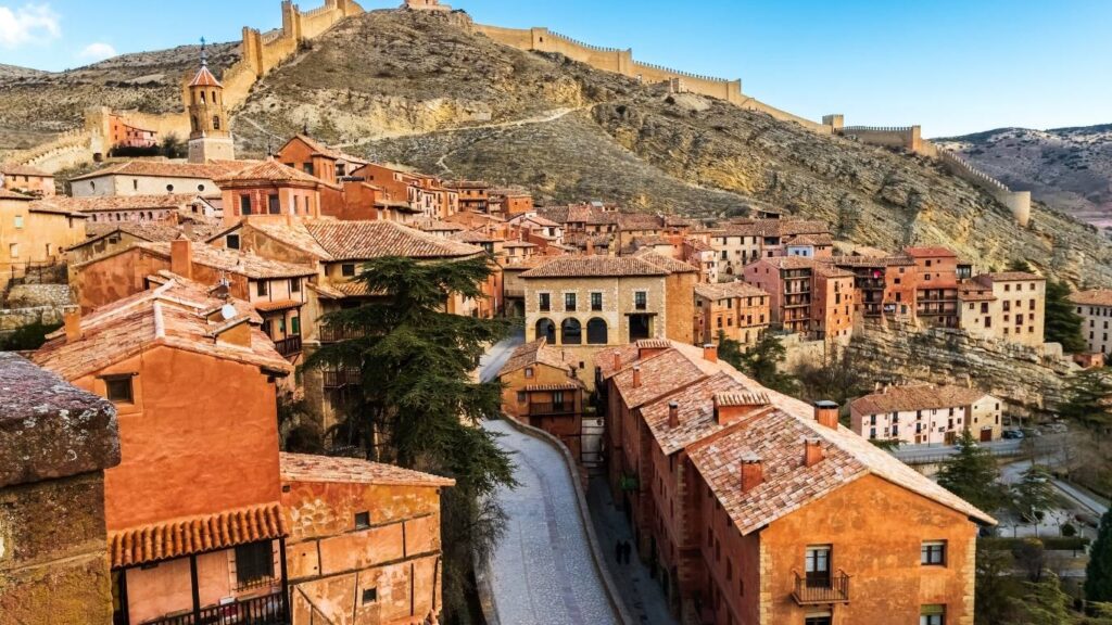 Calle principal de Albarracín con casas de fachadas rojizas y el camino que sube hacia las murallas.