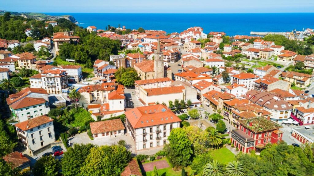 Fotografía aérea del centro histórico de Comillas con tejados rojos y la iglesia de San Cristóbal.