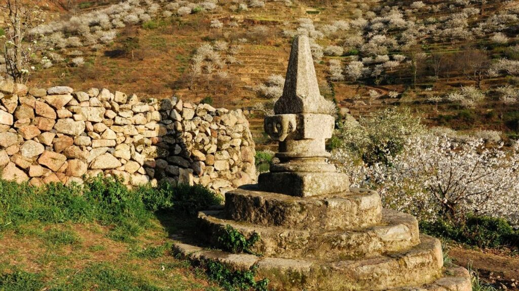 piedra antigua con forma de columna y remate cónico (conocido como "Las Marirrollas") situado junto a un muro de piedra rústico.