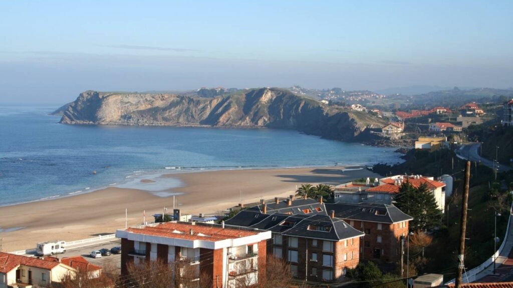 Playa de Comillas y acantilados al atardecer con edificios residenciales en primer plano.