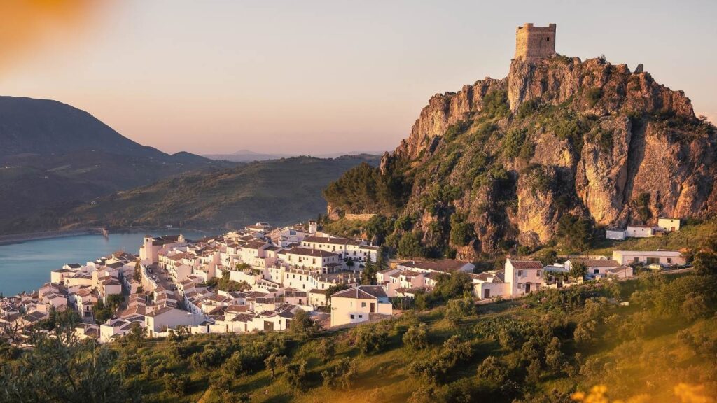 Vista panorámica de Zahara de la Sierra al atardecer con su castillo en la cima de la peña y el embalse al fondo.
